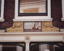 Klynschipper gild huys in Dordrecht. De Riedijk ligt direct achter de Merwekade, een logische locatie voor het gildehuis van de kleinschippers, één van de zes schippersgilden die Dordrecht telde. Er is een roeiboot en een zeilschip met spriettuig en voorzeilen afgebeeld.