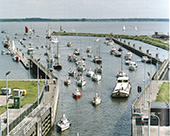 Druk recreatieverkeer in de voorhaven van de jachtensluis van de Volkeraksluizen, circa 2000. De Volkeraksluizen, die in 1969 in bedrijf kwamen, vormen in ons land de enige scheepvaartverbinding tussen het populaire watersportgebied Zeeland en de rest van ons land. In 1977 werd het sluizencomplex uitgebreid met een derde schutkolk voor de beroepsvaart en een aparte sluis voor de snel groeiende recreatievaart. Omstreeks 2010 passeerden door de Volkeraksluizen jaarlijks ongeveer 115.000 vrachtschepen en 45.000 pleziervaartuigen.