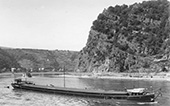 Rijnsleepschip <em>Saturnus</em> op sleep op de Duitse Rijn bij de bekende berg de Loreley, circa 1950. In de Rijnvaart gold de goede traditie dat bijna iedere reder de vaartuigen die hij aan zijn vloot toevoegde op deze karakteristieke locatie fotograferen. Tegenwoordig beschikken we daardoor over een groot aantal Loreley-scheepsfoto’s. De Saturnus voldeed aan de standaardafmetingen van een zogenaamd Rijn-Hernekanaalschip, met een lengte van 80 meter en een laadvermogen van 1.350 ton.