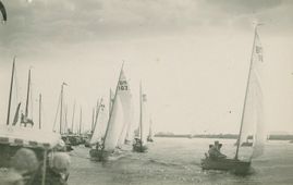 Vijftien BMers vlak na start tijdens een zeilwedstrijd in Akkrum, 1931. De nummers 16 en 103 zeilen in de richting van de fotograaf, die zich tussen het publiek bevindt. De foto is vermoedelijk gemaakt door een amateurfotograaf met een boxcamera. Net als de watersport, bereikte tijdens het interbellum ook de fotografie de massa.